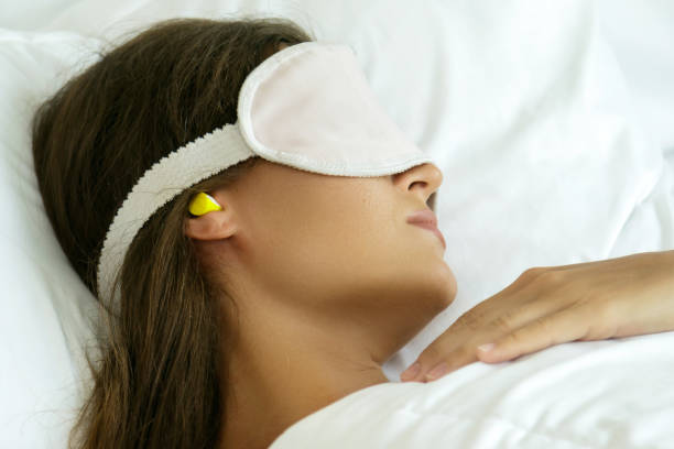 Une femme porte un masque pour les yeux et utilise des bouchons d'oreille pour mieux dormir.