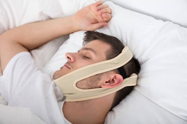 Jeune homme dormant avec une mentonnière anti-ronflement sur la tête à la maison pour trouver un bon sommeil.